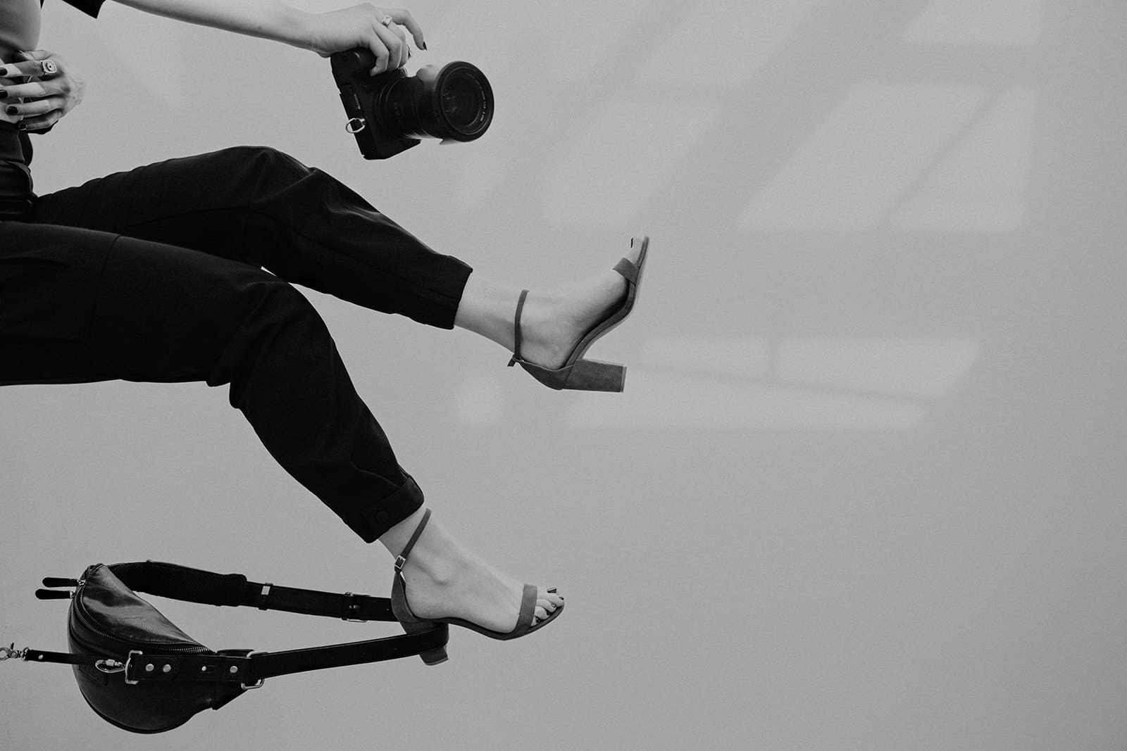 Photo of legs in heels in the air with a camera in one hand and a bag hanging off the heel of the shoe